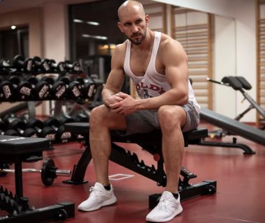 Strong, determined man in white tank top sitting in gym, showcasing fitness and strength.